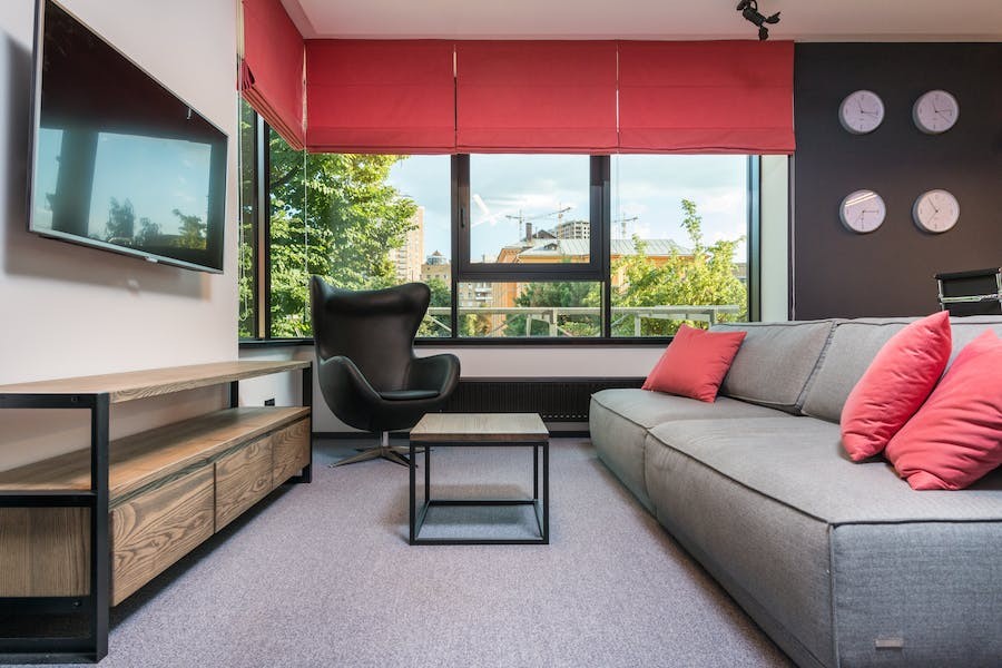 A modern home office interior featuring a couch, television, and red motorized shades on the windows.